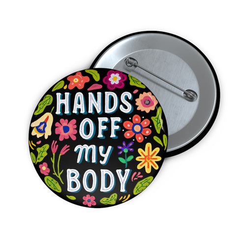 Glossy black pinback button with floral art and bold white text that reads “Hands Off My Body.” Feminist political button featuring bright pastel flowers in pink, red, orange, and yellow. Metal pin with durable safety pin back, shown in various settings: held by hand, displayed on pedestal, and against colorful street art. Available in 2" and 3" sizes, perfect for backpacks, jackets, tote bags, or as a gift for feminist allies and book lovers.