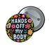 Glossy black pinback button with floral art and bold white text that reads “Hands Off My Body.” Feminist political button featuring bright pastel flowers in pink, red, orange, and yellow. Metal pin with durable safety pin back, shown in various settings: held by hand, displayed on pedestal, and against colorful street art. Available in 2" and 3" sizes, perfect for backpacks, jackets, tote bags, or as a gift for feminist allies and book lovers.