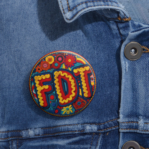 Round pinback metal button featuring an embroidered-style design on a vibrant, multicolored background. The bold, textured letters "FDT" are prominently displayed in red with intricate golden-yellow stitching details, outlined in dark blue. Surrounding the text is an ornate floral pattern with embroidered-style flowers in shades of red, orange, blue, and yellow, densely arranged for a rich, decorative effect. The outer edge is bordered with a zigzag stitching effect in red and blue. The button's back is sil