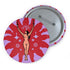 Circular pin featuring a nude goddess figure in gold against a red sunburst pattern on lavender background, with moon and star details
