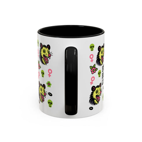 Possum Feminist Feral Before Coffee Mug (11, 15oz) features a bold, punk-themed design of neon opossum heads, green skulls, and feminist symbols. Ideal quirky gift for goth, neurodivergent, non-morning people. Dishwasher and microwave safe.