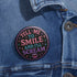 Glossy black pinback button with pastel-colored embroidered-style text that reads “Tell Me to Smile and I’ll Scream,” with lips icon and star accents.