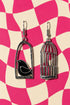 two silver earrings with bird designs, one in a cage and one without a cage, set against a pink and white checkered background.