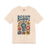Cream unisex t-shirt featuring a centered design with dark teal raised fist surrounded by folk art botanical elements: crimson and red 5-petal daisies, golden yellow and orange flowers, cornflower blue petals, and small scattered wildflower accents arranged in a symmetrical medallion composition. Dark teal "RESIST" text appears above the fist. The design uses faux embroidery 2D print with dimensional texture detail. Shown on unisex fit with ribbed knit collar and short sleeves.