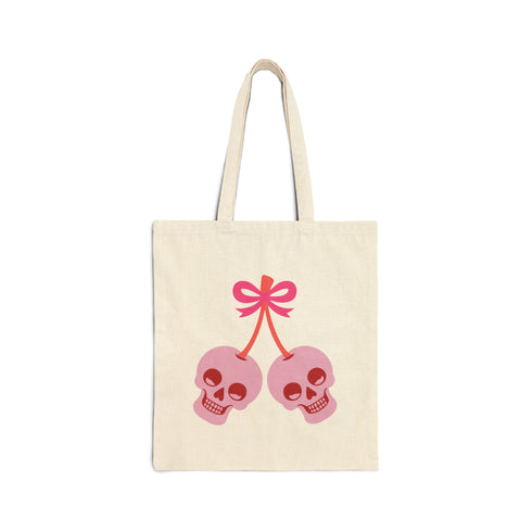Canvas tote bag featuring pink skull cherries design. Two pink skulls connected by red stem and bow. Quirky gothic-inspired graphic on cream background. Stylish, edgy accessory for everyday use. Perfect for alternative fashion lovers.