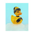 A chic rubber duck styled like Audrey Hepburn’s Holly Golightly, wearing a high bun, yellow bow, black gloves, and a sparkly choker. The duck floats in a pile of foam and is framed in white on a bubbly bathroom shelf with a red tile backdrop and soap dispenser.
