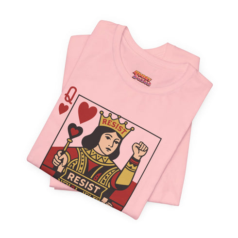 A centralized graphic design of a Queen of Hearts playing card on a cream or pink unisex t-shirt. The Queen is depicted in a maximalist folk art style, holding a heart-topped scepter and a raised fist in a gesture of solidarity. The word "RESIST" is visible on her crown and a central banner in ochre and true red tones. The layout is a centralized medallion style with rust and ochre accents and a playing card border.