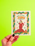 A 5x7 pearlescent holiday card by HoneyDazed. The card illustration, inspired by John Waters, features the drag queen Divine in a red dress with a Santa hat. She points a gun, withtext reads "Have Yourself a Filthy Christmas" in campy font. The card is bordered by garland. Iinside of the card reads: "Season's Sleazings" in red and green text. This kitschy greeting card is a perfect piece of cult film memorabilia and a funny adult humor gift for fans of queer art.