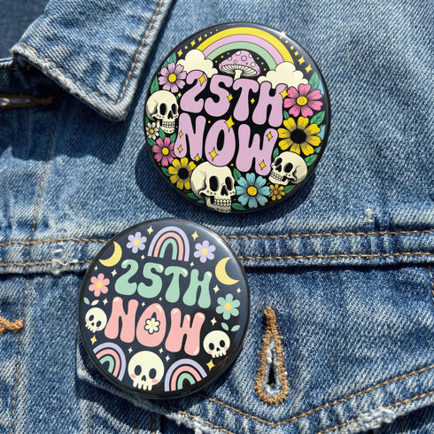 A round pinback button featuring a solid black background covered in a retro pastel colored design. The center reads 25TH NOW in a groovy bubbly font using pale pink and mint green referencing the 25th amendment. Surrounding the text is a maximalist cluster of cute but edgy motifs including smiling white skulls, pastel rainbows, pale yellow crescent moons, daisies, and a pink and white spotted mushroom. The button has a glossy laminate finish and a secure metal safety pin backing.