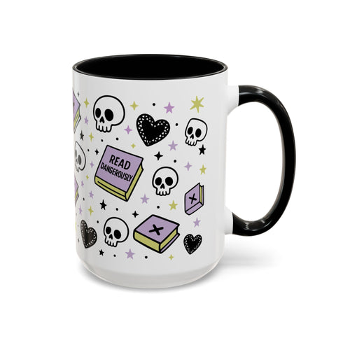 The Gothic Read Dangerously Mug Accent Coffee Mug (11, 15oz) features a glossy ceramic finish, black handle and rim, and is decorated with skulls, hearts, stars, books, and “READ DANGEROUSLY” in black, purple, and yellow.