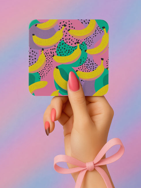 Square drink coaster featuring a playful banana print with bold yellow bananas over a pastel pink, purple, and green abstract background. Made of durable hardboard MDF with a cork backing and a glossy protective topcoat. Measures 3.74 by 3.74 inches, water-repellent and heat-resistant. Perfect for fruit-themed, retro, Y2K, coquette, or dopamine-core decor styles.t