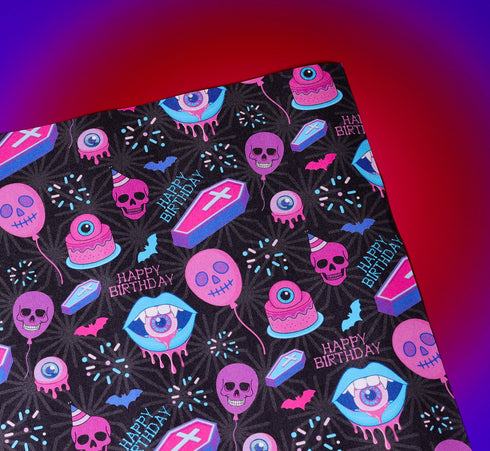 Spooky birthday wrapping paper with neon pink skulls, blue coffins, eyeballs, and bats on black background. Vibrant and gothic design for unique gift presentation.