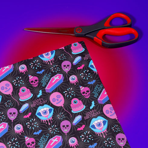 Spooky birthday wrapping paper with neon pink skulls, blue coffins, eyeballs, and bats on black background. Vibrant and gothic design for unique gift presentation.