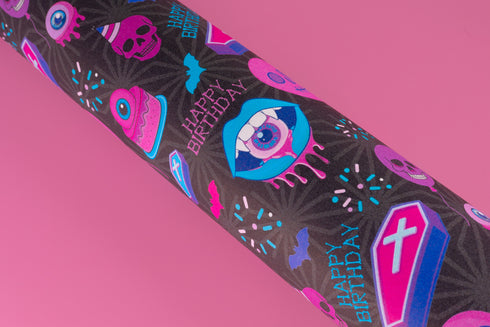 Spooky birthday wrapping paper with neon pink skulls, blue coffins, eyeballs, and bats on black background. Vibrant and gothic design for unique gift presentation.
