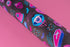 Spooky birthday wrapping paper with neon pink skulls, blue coffins, eyeballs, and bats on black background. Vibrant and gothic design for unique gift presentation.