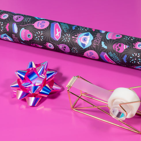 Spooky birthday wrapping paper with neon pink skulls, blue coffins, eyeballs, and bats on black background. Vibrant and gothic design for unique gift presentation.