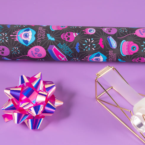 Spooky birthday wrapping paper with neon pink skulls, blue coffins, eyeballs, and bats on black background. Vibrant and gothic design for unique gift presentation.