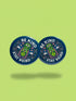 A round 1.75 inch pinback button featuring a retro psychedelic design on a dark navy blue background. The text reads BE KIND STAY WEIRD in vintage cream lettering around the border. The center illustration depicts a neon green skull stacked on top of a neon green alien head. Both the skull and alien have opening third eyes on their foreheads. Pink wavy lines frame the faces. The background is decorated with small colorful mushrooms, hearts, stars, and clouds. Glossy finish.