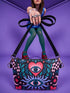 Small vegan leather crossbody purse with a real pebble grain texture and adjustable black strap. The flat printed artwork features a central blue sunburst evil eye motif below a coral pink sacred heart eye, surrounded by pink crescent moons, multicolored stars, flowing teal botanical vines, and wavy lavender and black checkerboard distortion banners. Set against a dark background with silver metal hardware including a top zipper, zipper pull, and strap clips. Measures 8.5 by 7 by 2 inches.