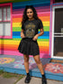 A black unisex crewneck graphic t-shirt featuring an ornate Victorian-inspired emblem printed on the chest in vintage gold and off-white. The centralized, symmetrical design showcases a classic coffin with a cross on the lid, flanked by wrought-iron cemetery gates. Beautiful scrollwork and decorative filigree flourishes surround the bold, retro serif text reading CEMETERY PICNIC SOCIETY. A crescent moon and stars sit at the top, completing this gothic memento mori graphic shirt.