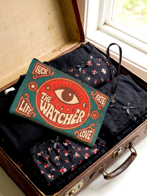 A rectangular 9x6 inch makeup bag and zipper pouch featuring a textured linen-like polyester fabric. The bag showcases a bold, maximalist print with vivid colors typical of retro 70s and pastel goth aesthetics, centering on a large mystic eye design labeled "The Watcher." It features a sturdy black zipper across the top and includes a removable black nylon wristlet strap.Perfect for use as a pencil case, cosmetic organizer, or festival wristlet.