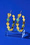 A pair of gold earrings with turquoise stones, displayed on a clear glass stand against a blue background.