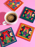 A set of four square coasters featuring a glossy glazed finish and vibrant insect illustrations. Each coaster measures approximately four by four inches. The designs showcase symmetrical beetles and spiders in bold red, blue, and orange colors, framed by intricate floral and geometric borders in a maximalist folk art style. Available in ceramic with cork backing or hardboard MDF. The edges are smooth. The designs are vivid and highly saturated, designed to provide grip and protect furniture.