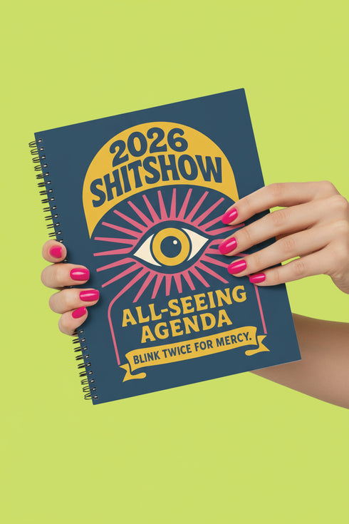 A hardcover spiral planner for 2026 with a dark blue cover and retro 70s style graphics. The title reads "2026 SHITSHOW All-Seeing Agenda" in bold yellow and pink text. Below the title is a large, stylized all-seeing eye with pink rays emanating from it. At the bottom, a pink ribbon contains the text "BLINK TWICE FOR MERCY." The back cover is also dark blue with a yellow sun graphic and the text "Plans bloom. Deadlines hum. I write, I wander, then get it done. Keep receipts. Keep grace.