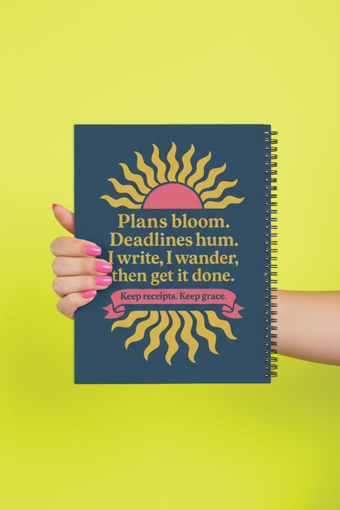 A hardcover spiral planner for 2026 with a dark blue cover and retro 70s style graphics. The title reads "2026 SHITSHOW All-Seeing Agenda" in bold yellow and pink text. Below the title is a large, stylized all-seeing eye with pink rays emanating from it. At the bottom, a pink ribbon contains the text "BLINK TWICE FOR MERCY." The back cover is also dark blue with a yellow sun graphic and the text "Plans bloom. Deadlines hum. I write, I wander, then get it done. Keep receipts. Keep grace.