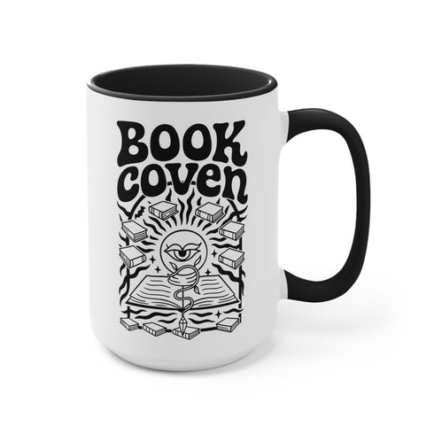 A two-tone ceramic mug with a glossy white exterior and a contrasting black interior, handle, and rim. The front of the mug features a black, rectangular graphic with the words "BOOK COVEN" in a bold, wavy, 70s-inspired retro font. Below the text is an occult-style illustration of an open book on a stand. An all-seeing eye with a snake coiled around it emerges from the book's pages, radiating lines of light. Smaller books float around the central image, completing the witchy, bookish design