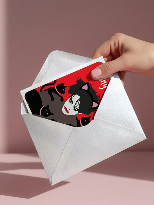 A vertical greeting card featuring a flat vector illustration of Robert Smith from The Cure against a vibrant red background. He has messy black hair, pale skin with smeared lipstick, and wears black cat ears. He is surrounded by four black cats with pink collars. White script text at the top reads "Be my Lovecat." The card is printed on shimmery pearlescent cardstock that catches the light. A high-quality alternative Valentine or anniversary card for goth music lovers and post-punk fans.