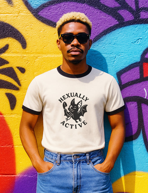 Unisex offwhite and black ringer t-shirt with a bold black graphic of a cartoon bat holding a wand, surrounded by the phrase “Hexually Active.” The design is playful, witchy, and gothic, perfect for lovers of magic, spellwork, hexes, and witch humor. The shirt features contrast collar and sleeves in black for a retro vibe.