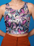 A sleeveless cropped tank top made from stretchy performance knit fabric. The all-over print features a dense, scattered pattern of pastel goth and creepy cute motifs over a light background. Graphics include pink and blue bats in flight, floating eyeballs with blue irises, pink skulls, and glossy vampire lips with sharp white fangs and tongues sticking out. The neckline is a high scoop and the armholes are curved. The fabric comes in either a matte finish or a sparkly silver glitter foil.