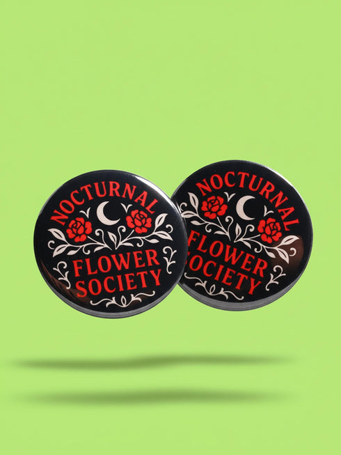 A collection of four glossy black circular pinback buttons featuring striking red and white gothic illustrations. One button shows "Midnight Graveyard Society" text with bats and tombstones. Another reads "Cemetery Picnic Society" with a coffin and umbrella icon. A third features a detailed white skull and red roses with "Memento Mori" text below. The final pin displays "Nocturnal Flower Society" surrounded by floral vines.