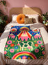 A rectangular velveteen minky blanket with a bright, maximalist design. The top half features a vibrant blue sky with a pink, green, and yellow UFO beaming rays down over hot pink snow-capped mountains. The bottom half shows a grassy green field with a white cow covered in dark spots, surrounded by large, colorful red, pink, and blue retro flowers, pine trees, and a rainbow arch at the very bottom. The reverse side is a fluffy off-white sherpa.