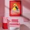 A spooky-yet-cute art print of a vampire-themed rubber duck dressed in a red-lined black cape and bowtie. Surrounded by white bath bubbles, the duck is framed in a red wavy-edged frame and held up against a burnt orange wall by a hand in a dramatic red sleeve.