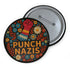 Round black pinback button with bold embroidered-style design featuring a raised red fist, zigzag sleeve, and colorful folk art flowers in orange, teal, yellow, and white. Center text reads “PUNCH NAZIS” in bright golden thread-style lettering. The design is bold, anti-fascist, and maximalist, shown on a glossy pin surface against a pink and purple gradient background. Statement accessory for protest fashion, punk style, and political activism.