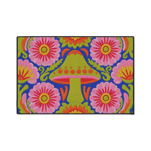 A rectangular polyester mat featuring a large central mushroom with a lime green cap, orange spots, and a pink underside. The design is surrounded by four large magenta and pink radial flowers with yellow centers. Bright green leaves and orange scrolling vines fill the spaces on a deep cobalt blue background. The artwork uses a tapestry-style visual effect to mimic the look of raised embroidery on a flat, printed surface. The mat is finished with a clean black stitched edge.