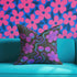 Square throw pillow with a black background featuring a psychedelic pattern of bright pink cherries, purple hibiscus flowers, and wavy teal and magenta lines. Design is bold, colorful, and maximalist.