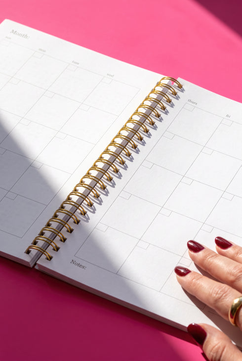 An open spiral-bound notebook with a blank page is shown, with a person's hand resting on the right side of the page.
