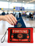 A rectangular red zippered pouch featuring a vintage-style tarot card design. The front displays the word FORTUNE in large beige capital letters. A central illustration shows a mystic eye emitting rays of light above a lit candle flame. The text YES and NO appears on the sides. A banner at the bottom reads LIGHT IT TO KNOW. The bag is crafted from red polyester with a linen-like woven texture, featuring a black zipper and a removable black nylon wrist strap. The interior is white.
