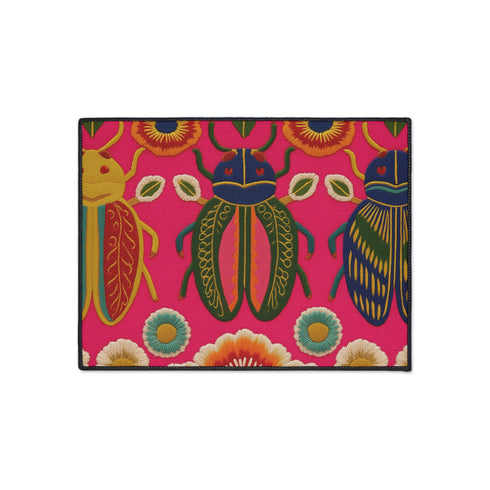 A rectangular doormat featuring a vibrant hot pink background with a high-fidelity tapestry-style print of three large, detailed beetles. The central beetle is emerald green and gold with navy accents, flanked by two side-profile beetles in ochre and deep blue. Stylized teal and yellow sunburst flowers and small sage green leaves are scattered throughout the design. The mat has a sleek black-trimmed edge and a visible flat, durable polyester texture mimicking intricate needlework.