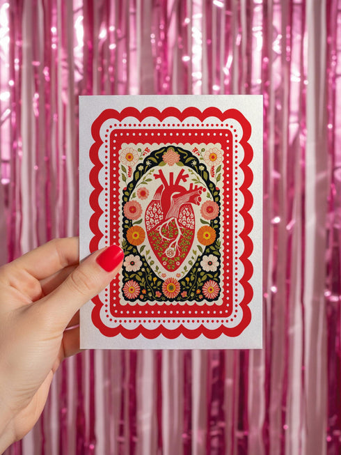 Realistic anatomical heart illustration printed in high contrast ink on a premium 5x7 inch shimmery pearlescent greeting card. The biological heart drawing features detailed arteries, veins, and ventricles, styled with a vintage medical or folk art aesthetic. The cardstock has a visible iridescent sheen. Blank inside valentine card shown with a white peel and seal envelope. Perfect for gothic decor, medical student gifts, cardiology nurse appreciation, and dark academia stationery collections.