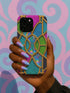 A hand holding a colorful phone case with a stained glass design against a background of swirling pink and blue patterns.