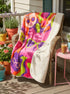 A rectangular velveteen minky blanket with a bright, retro pop art design. The top features a large, hot pink cat head wearing lime green sunglasses in the center. Swirling psychedelic background rays in vibrant orange, purple, and lime green radiate outward. Four smaller cat heads in peach, green, and purple, also wearing glasses, sit in the corners alongside retro flowers, stars, and a lime green heart. The reverse side is a fluffy off-white sherpa fleece.