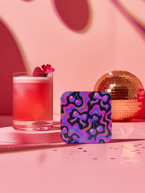 Square drink coaster featuring a bold Y2K-inspired pattern with gradient cherries and shiny pink bows on a black background with psychedelic pink, purple, and blue squiggle lines. Made from hardboard MDF with a non-slip cork backing and a high-gloss topcoat. Measures 3.74 by 3.74 inches. Water-repellent and heat-resistant, ideal for pastel goth, coquette, maximalist, and dopamine decor themes.