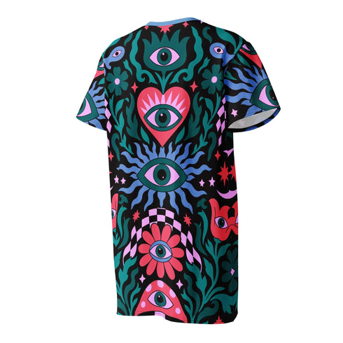 A short-sleeve, above-the-knee t-shirt dress with a true black background. The front features a vibrant, vertically stacked symmetrical graphic design. From top to bottom, the design includes a pink heart containing a green and blue eye, a large blue sunburst with a central eye, a red daisy flower with an eye flanked by pink and black checkered arches, and a pink mushroom cap with an eye. Swirling emerald green foliage, pink stars, and purple stars fill the negative space around the motifs.