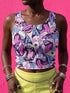 A sleeveless cropped tank top made from stretchy performance knit fabric. The all-over print features a dense, scattered pattern of pastel goth and creepy cute motifs over a light background. Graphics include pink and blue bats in flight, floating eyeballs with blue irises, pink skulls, and glossy vampire lips with sharp white fangs and tongues sticking out. The neckline is a high scoop and the armholes are curved. The fabric comes in either a matte finish or a sparkly silver glitter foil.