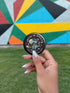A hand holding a round object with a colorful geometric design in front of a colorful mural.