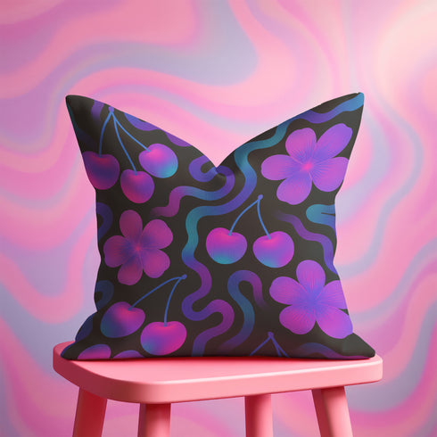 Square throw pillow with a black background featuring a psychedelic pattern of bright pink cherries, purple hibiscus flowers, and wavy teal and magenta lines. Design is bold, colorful, and maximalist.